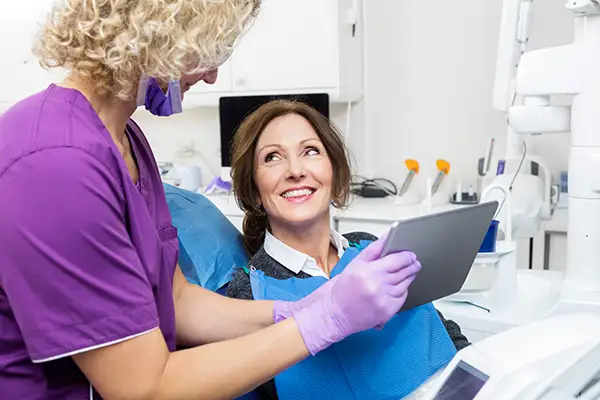 A smiling female patient interacting with her dentist, who is holding a tablet to explain her tori removal procedure.