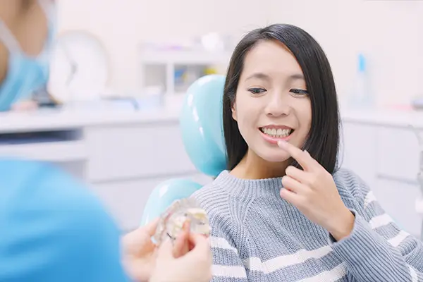 Doctor explaining the process of dental implant to a patient, while the patient is in dental chair holding her finger towards her tooth.